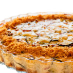 Close-up of homemade crustless zucchini quiche baked in a glass fluted dish isolated on white